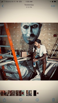 a man sitting on a ladder next to a mural